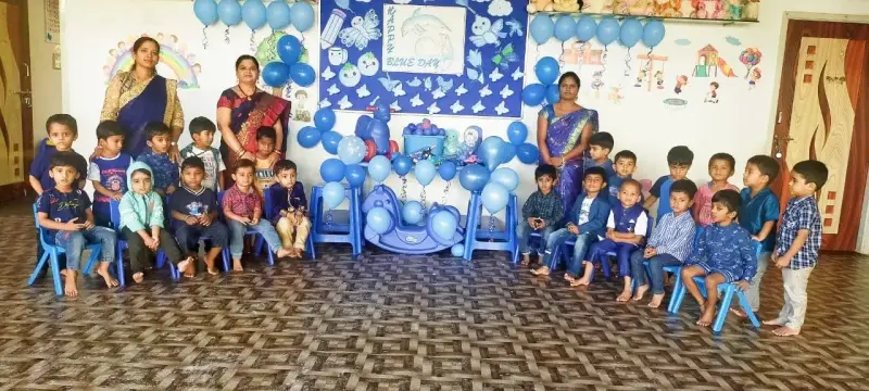 Young children dressed in blue sit with three adults in front of a Blue Day display and blue balloons.