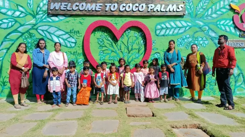 Young children and adults stand in front of a painted wall that reads Welcome to Coco Palms.